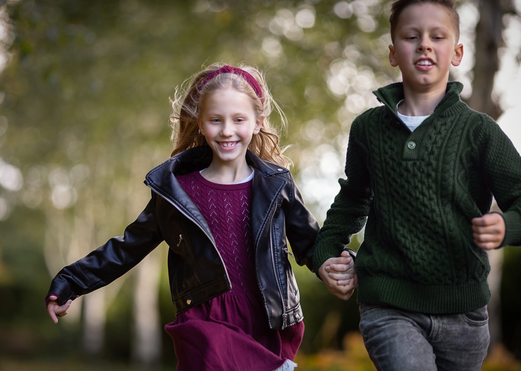 Brother and sister running hand in hand during an outdoor family photoshoot in Glasgow at Pollok Country Park