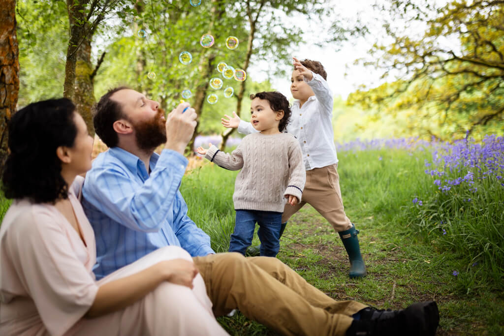Parents blowing bubbles as their children try to catch them on a meadow during a family photoshoot in Glasgow