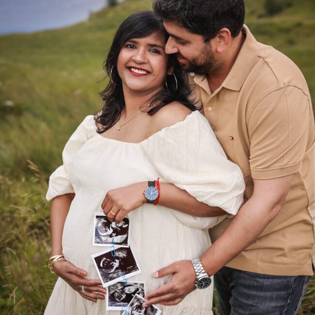 Expectant couple holding ultrasound scan photos against the woman's baby bump during an outdoor maternity photoshoot in Glasgow