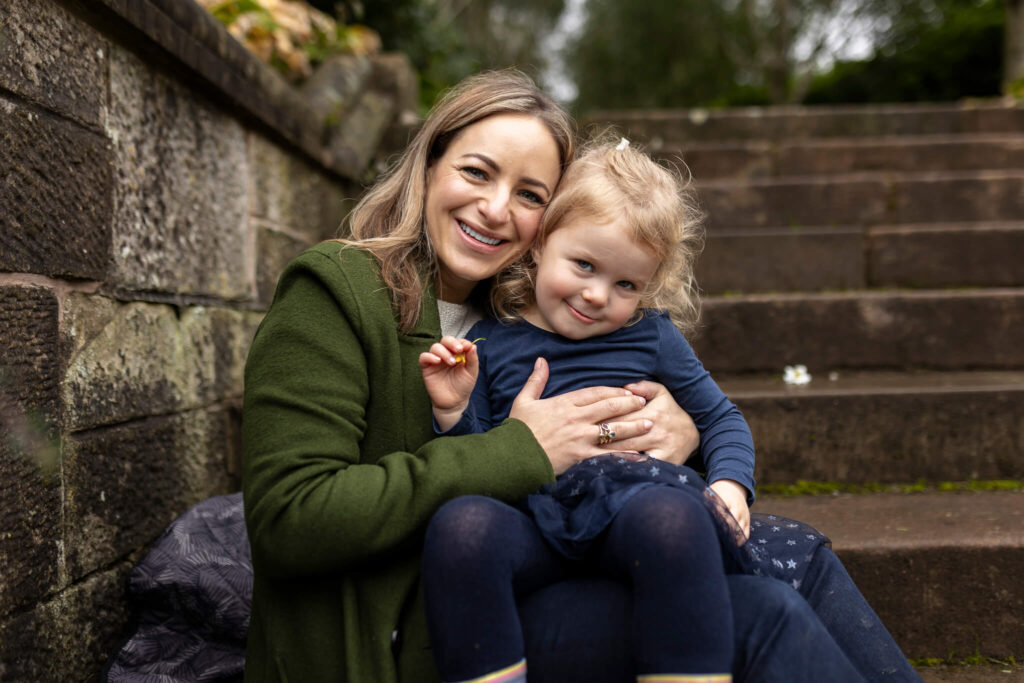 Mother and daughter sitting on steps with her daughter on her lap, smiling at the camera during a family photoshoot in Glasgow