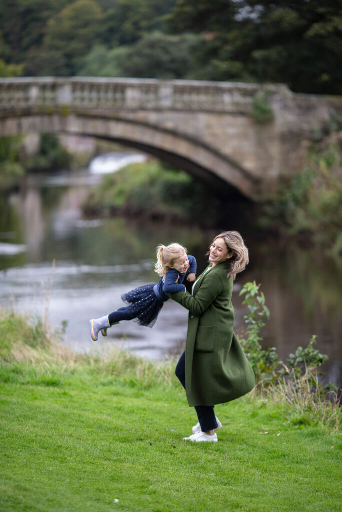mum swinging her child by the river and stone bridge during an outdoor family session