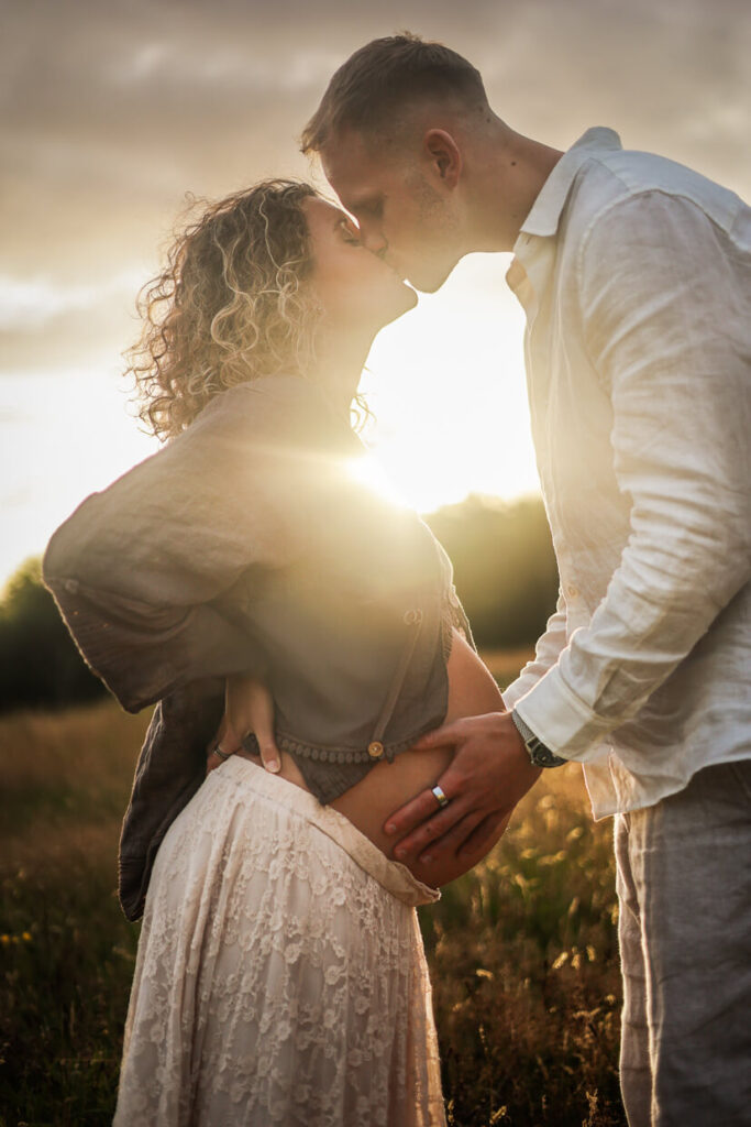 Couple kissing at sunset on a meadow during a maternity photoshoot in Glasgow, with the man holding her bump