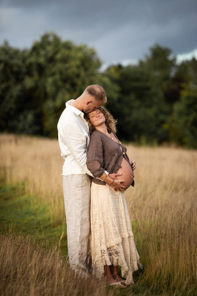 Couple embracing at sunset during a maternity photoshoot in Glasgow, with the woman leaning against her partner as he holds her bump