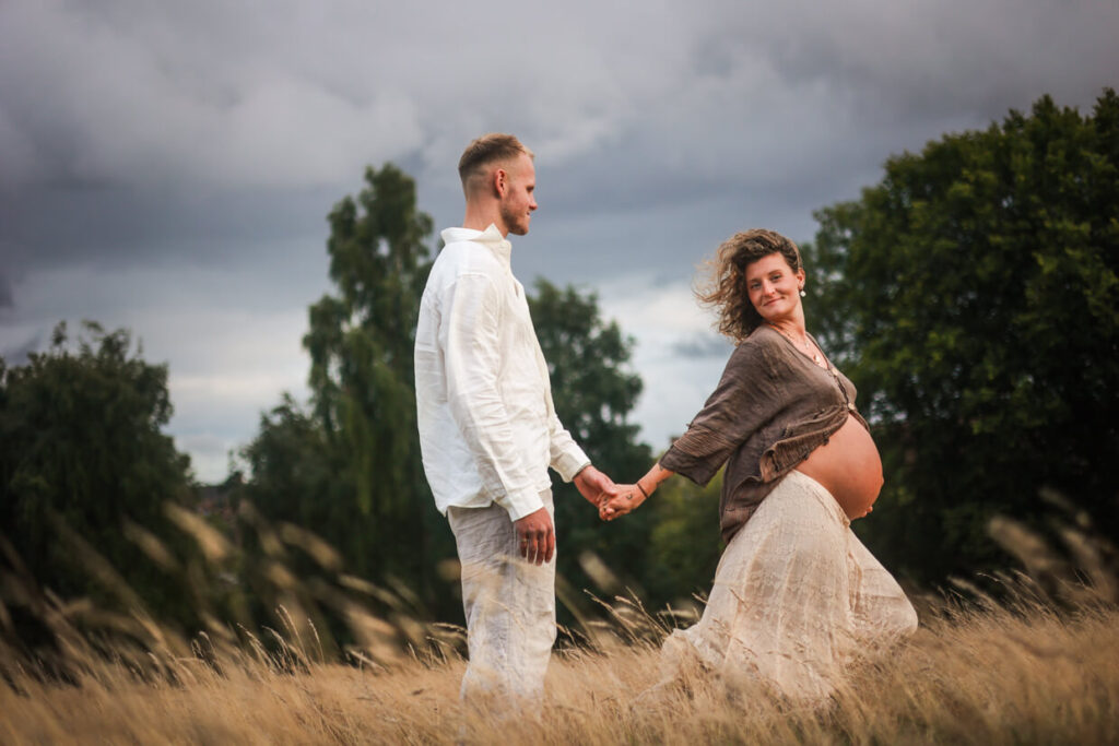 Couple in neutral beige and white outfits during an outdoor maternity photoshoot on a windy meadow in Glasgow