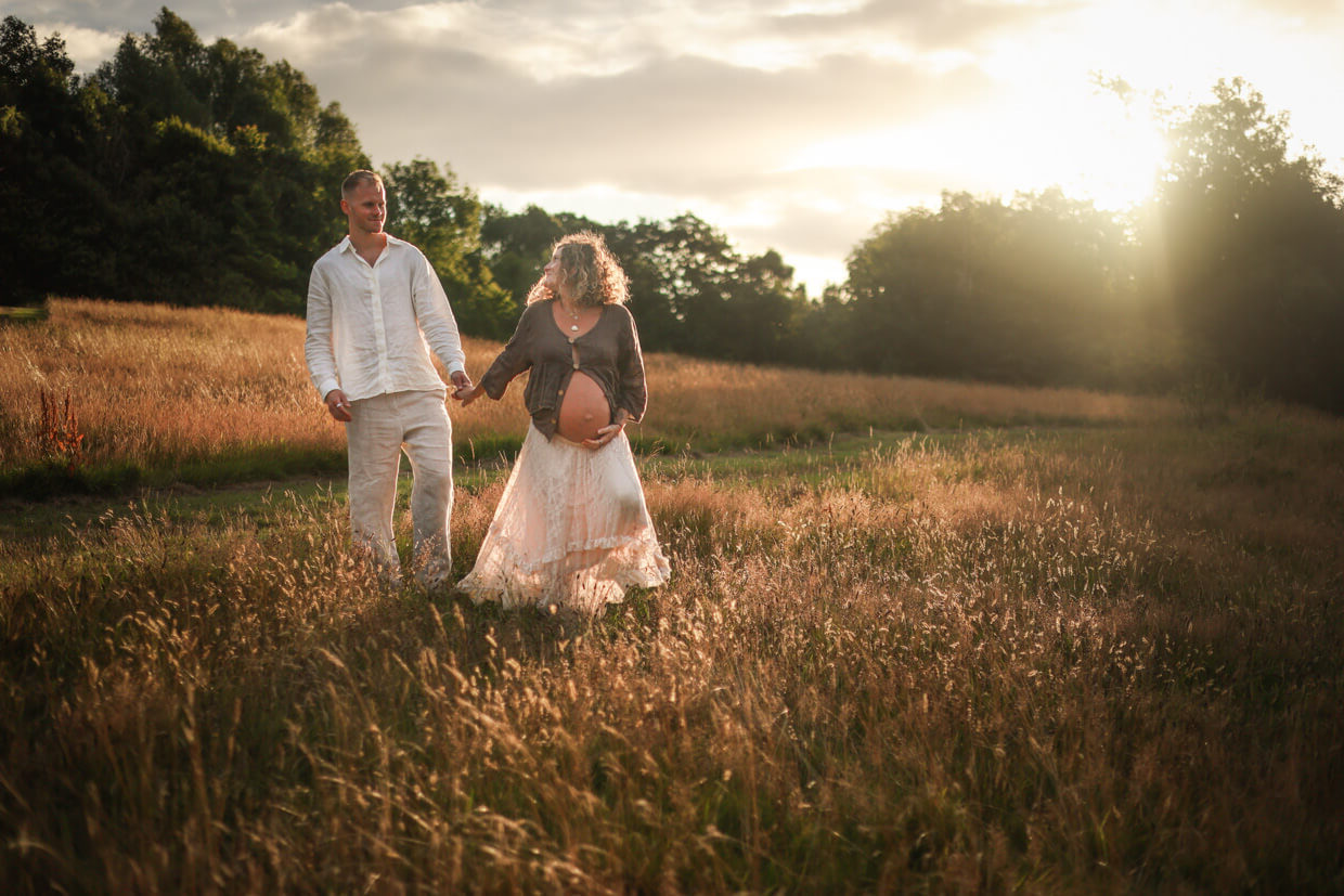 Expectant couple walking hand in hand through golden grass at sunset during an outdoor maternity photoshoot in Glasgow