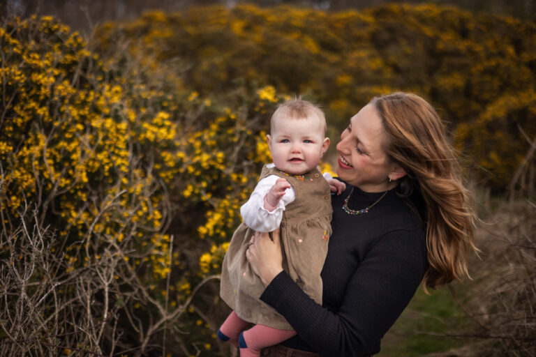 Mother holding her baby among yellow flowers during an outdoor baby photoshoot in Glasgow