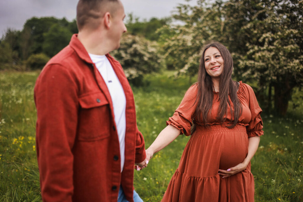 Expecting couple walking hand in hand through a blooming garden during an outdoor maternity photoshoot in Glasgow