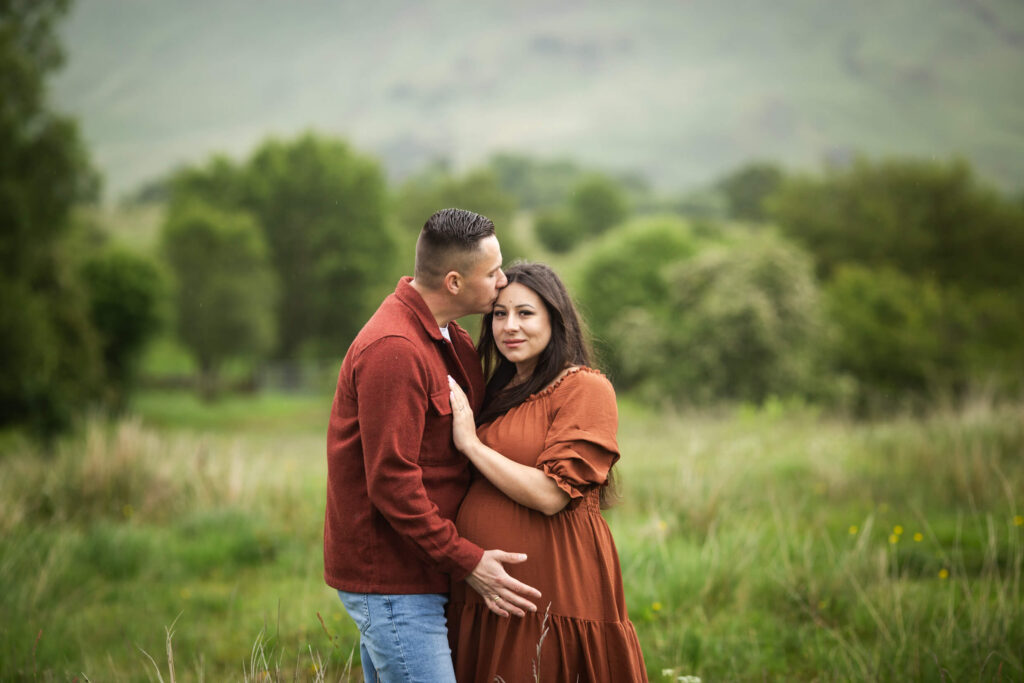 expecting couple embracing in a green field during a maternity photoshoot in Scotland
