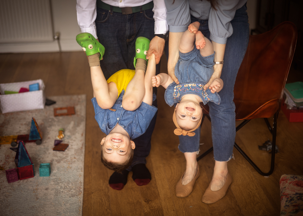 Parents playfully holding their two young children upside down during an at-home family photoshoot in Glasgow