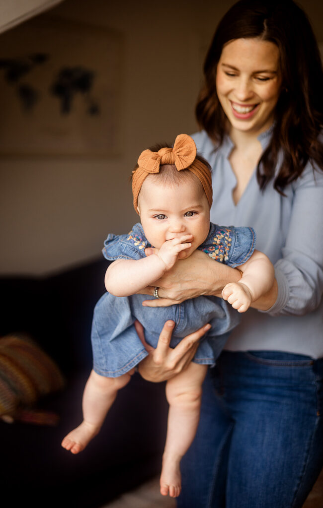 Mother holding her baby daughter as she looks at the camera with her fingers in her mouth during an at-home family photoshoot in Glasgow