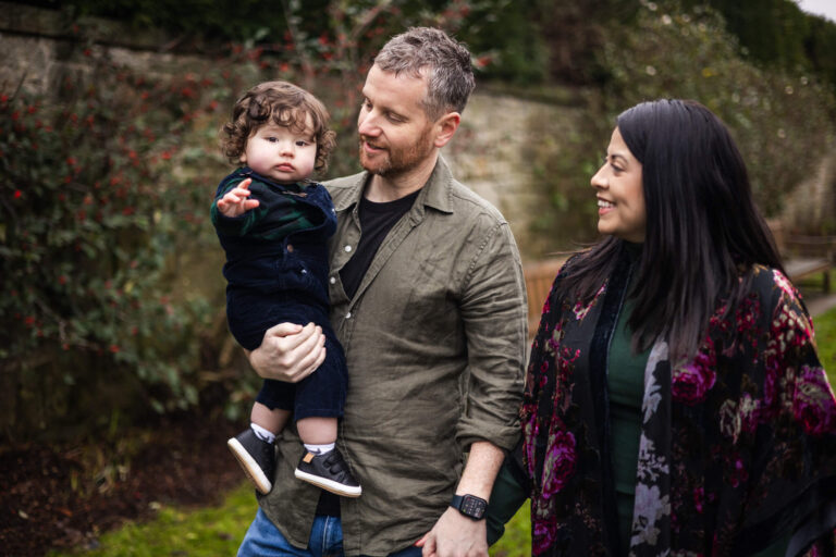 Father holding his young child while mum looks on during an outdoor family photoshoot in Glasgow