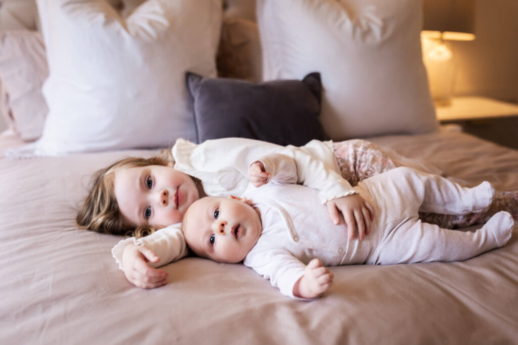 Toddler sister and baby brother cuddling together on the bed during an in-home newborn photoshoot