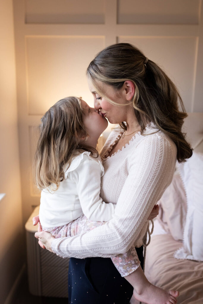 Mother cuddling and kissing her young daughter on the bed during an at-home family photoshoot in Glasgow