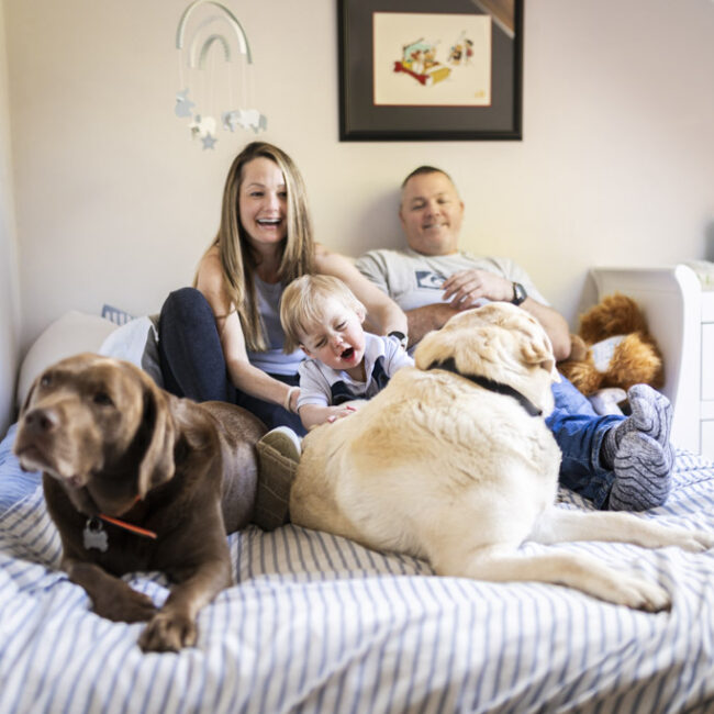 Parents relaxing on the bed with their young son and two family dogs during an at-home family photoshoot in Glasgow