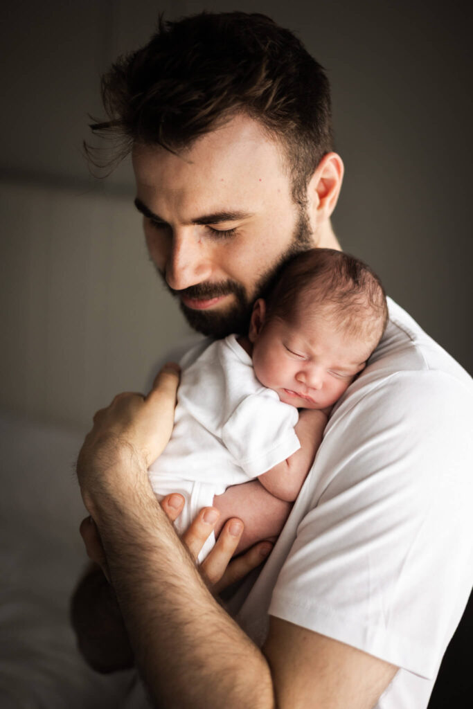 Dad holding his sleeping newborn baby against his chest at home