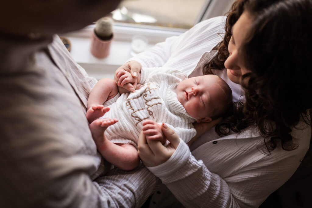 Overhead view of a newborn baby wearing a Hello World outfit while resting in mum's and dad's arms