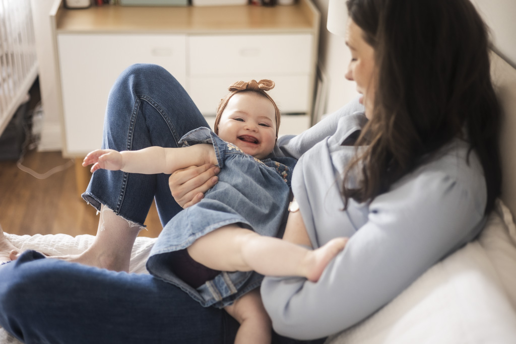 Mother holding her smiling baby daughter in a denim dress during an at-home family photoshoot in Glasgow